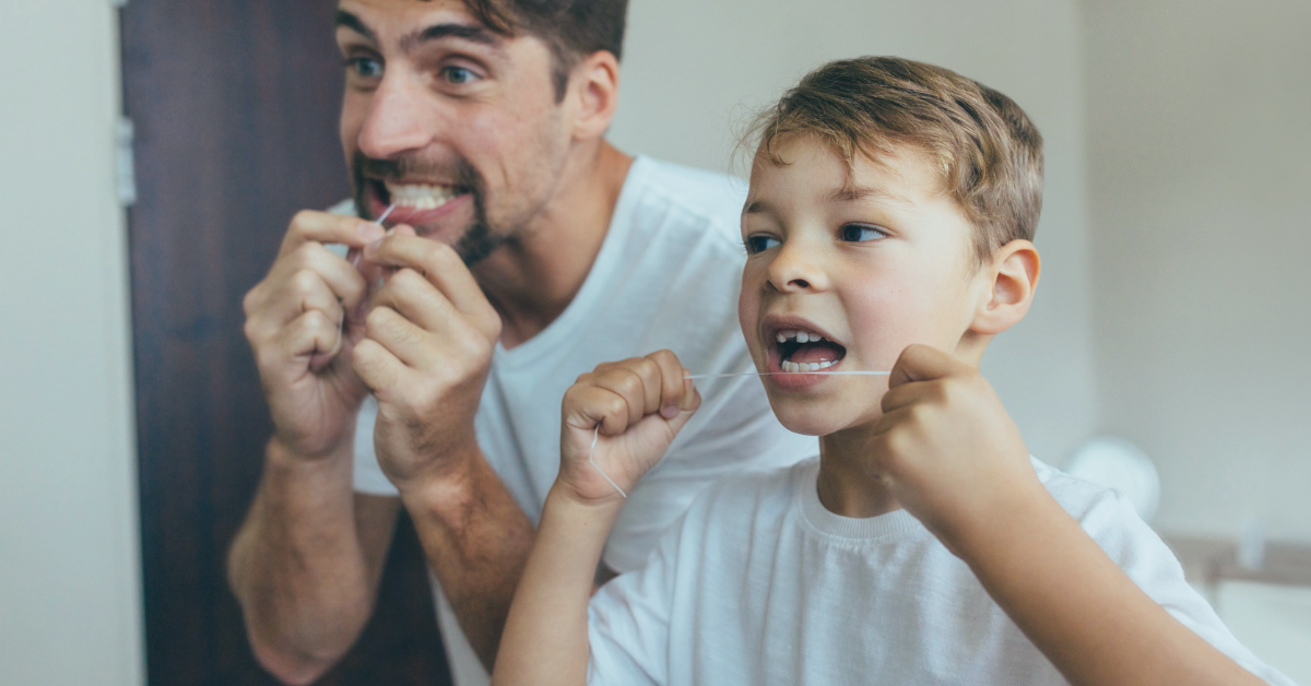Dad and son looking in the mirror and flossing their teeth. Saskatoon Dental Group How to Floss Your Children's teeth Feb Blog 